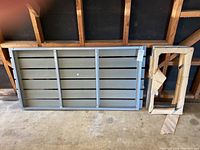 Disassembled table components laid on floor in a garage: tabletop and frame parts, gray color.