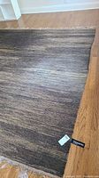 Full view of the brown gradient woven wool rug laid on hardwood floor with visible fringe and a label tag.