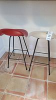 Pair of vintage molded plastic and metal stools with one red and one white seat with metal black legs on tiled floor.