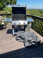 Front view of open Weber Genesis II grill on deck with cover folded beside it