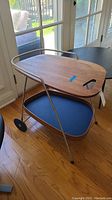Full view of two-tiered serving cart with wooden top and blue lower tray on wheels