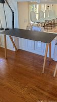 Black writing desk with wooden legs in room setting
