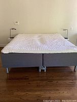 Front view of two grey upholstered bed bases joined as king size with white quilted pad.