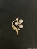 Front view of the gold pendant showing three pearls and a diamond chip arranged in a floral-like cluster with a decorative leaf design.