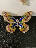 Close-up of colorful enamel butterfly brooch with rhinestones on black background.