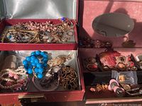 Red and pink vintage jewelry boxes filled with various vintage costume jewelry pieces showing bead necklaces, bracelets, brooches, and watches.