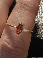 Close-up of silver ring with marquise red stone and smaller clear stones on finger showing details and style.