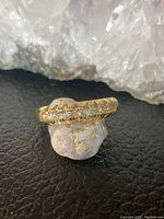 Front angled view of the gold tone band with clear stones, set against a natural stone background showing the thickness and stone setting.