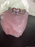 Front view of the silver and gold tone heart ring with purple stone placed on pink crystal.
