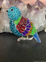 Close-up photo of blue parrot brooch with multi-colored enameled feathers and blue gems.