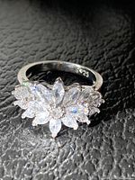 Close-up of silver ring size 6 stamped 925 with clear stones cluster design on black textured surface