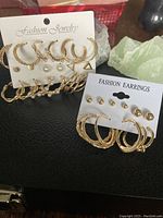 Photo showing multiple pairs of gold-tone hoop earrings and pearl stud pairs on display cards