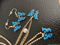 Close-up image showing earrings, pendant necklace, and bracelet with blue butterfly charms on a black background