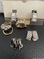 Five pairs of clip on earrings on a black surface with two pairs on a card display and others held and laid out.