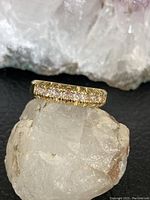 Front view of cubic zirconia ring on rough crystal showing heavy gold tone band and stone settings.
