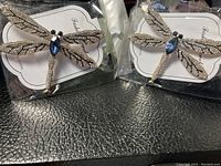 Photo showing both dragonfly brooches in packaging on black surface