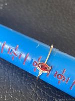 Close-up of gold tone ring showing red marquise stone and side cubic zirconia on size measuring stick at size 8.