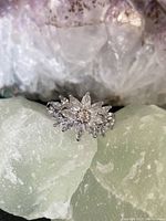 Close-up of the front face of the silver engagement ring with multiple clear cubic zirconia stones arranged in a floral design.