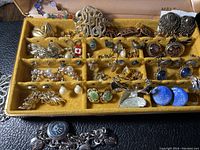 Close-up of vintage silver earrings in a velvet-lined yellow jewelry case showing various styles with precious stones and intricate designs.