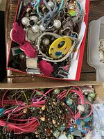 Top-down view of a box containing mixed crafting jewelry pieces including beads, pendants, chains, and fabric cords.