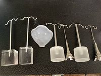 Five jewelry holders displayed on black surface. Two with clear square bases, two with frosted round bases topped with miniature Eiffel Towers, one with a scalloped clear base.