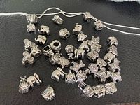 Photo showing animal-shaped silver coloured beads scattered on a black surface with a silver coloured chain.