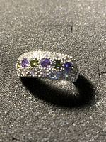 Close-up image of the silver ring showing alternating green and purple stones set in a sparkling pave design.