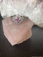 Close-up of sterling silver ring with square pink cubic zirconia center and clear cubic zirconia halo and band accents on pink stone background.