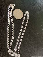 Silver chain necklace stamped 925 laid on black textured surface with a coin for size reference.
