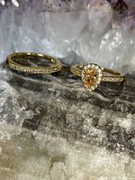 Two gold tone rings photographed on a textured rock surface, showing the shape and details of the citrine color stone and CZ accents.