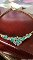 Close-up photo of gold-tone choker style necklace with blue and clear rhinestones placed on a wooden surface, showing front central decorative section