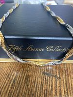 The twist chain necklace draped over the black Fifth Avenue Collection box, showing the gold and silver alternating pattern and scale-like texture.
