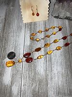 Amber necklace, bracelet, and earrings displayed together with a coin for scale and an amethyst crystal in the background.