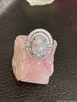Front view of sterling silver ring with oval opalescent moonstone and double halo of small clear stones on pink stone block.
