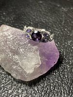 Mystic topaz ring resting on a rough amethyst stone showing the main stone and side details.