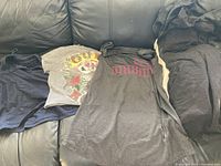 Overview of five teen girl clothing items on a couch, including T-shirts and pants in dark and gray colors.