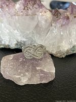 925 silver ring with multiple rows of small cubic zirconia stones arranged in a whimsical, interlaced pattern, displayed on a purple crystal rock with clear quartz cluster background.