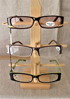 Image showing three pairs of rectangular reading glasses on wooden holder in black, brown and purple hues with clear lenses.