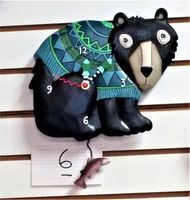 Front view of black bear clock wearing a blue and green sweater with the clock face on the sweater and a fish pendulum below.