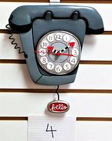 Full view of the gray rotary phone shaped wall clock with cord and "hello" pendulum visible.