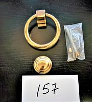 Top view of brass circle door knocker ring, dome base plate, and hardware bag on dark surface with lot number card.