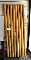 Eight tall bamboo poles standing upright, showing full length, consistent diameter, and natural bamboo characteristics.