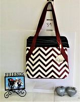 Full shot of the handbag hanging on a hook with the "Friends" picture frame and two heart decorations labeled "Dream" and "Happiness" below on a white surface