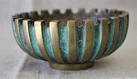 Side view showing the alternating polished bronze and greenish patina vertical stripes and scalloped rim with ashtray notches.