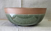 Side view of large ceramic bowl showing dark green glossy glazed body with light brown unglazed rim and shallow depth.