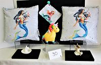 Two sequin cushions with mermaid design, unicorn and fairy figurines in background, small white unicorn head on display