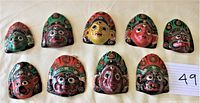 Top view of nine small vintage Nepali papier mache masks arranged in two rows on a white surface. The masks display various traditional artistic faces in colorful paint.