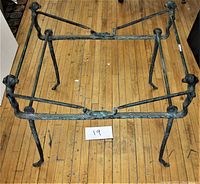 Full view of the rectangular bronze table base on wooden floor showing patinated finish and lion-head corner legs connected by twisted rods.