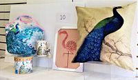 Photo of the peacock cushion, lunch bag, ceramic mug in keepsake box, and flamingo wall art, showing all items in lot.