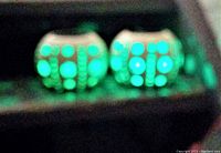Photo showing two cream-coloured ceramic solar lanterns emitting blue-green LED light through circular holes at night.